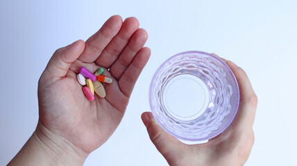 Patient woman holds medicine and a glass of water in hands, ready to take medicines with colorful pills, tablets and capsules for treatment the disease, prescription medication dosage from doctor.