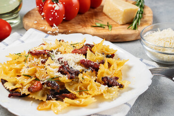 Sprinkling parmesan pasta with sun-dried tomatoes in a white plate on the table. Italian cuisine, ingredients and the finished dish