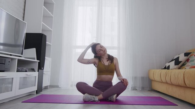 Young beautiful woman with tattoo stratching neck on mat at home