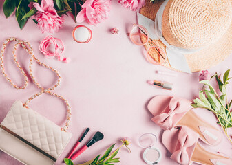 Pink female fashion background with pink peony flower, slippers, sunglasses, straw hat, bag and cosmetics.