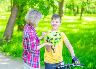 Activity family leisure. Mom gives her son a helmet for a safe ride on a bike