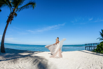 Fototapeta na wymiar Bride back view in a white wedding dress walking on the sandy caribbean beach landscape on sunny day in Dominican republic 