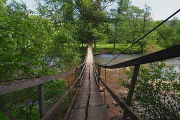Obraz premium Drewniany most wiszący nad rzeką płynącą w lesie. Letni krajobraz.