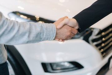 Buyer of car shaking hands with seller in auto dealership, in front of car. Close-up of handshake...