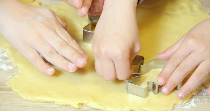 Closeup of children's and female hands carving cookies from dough using metal cookie cutters in a kitchen