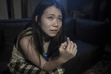 Asian girl suffering depression - sad and depressed Japanese woman crying in tears on darkness in pain worried and helpless at living room sofa couch overwhelmed by problem