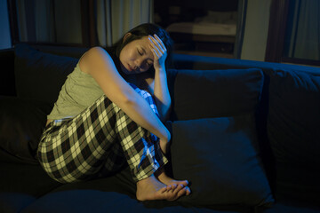 Asian girl suffering depression - sad and depressed Chinese woman crying on darkness in pain feeling worried and helpless on sofa couch overwhelmed by life problem