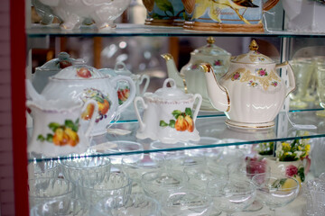 Display of antique tea pots and wine glasses on glass shelves