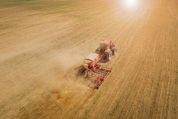 A tractor is working in a field with a plow. Plowing a field for sowing wheat. The dusty field in which the tractor works. Aerial view