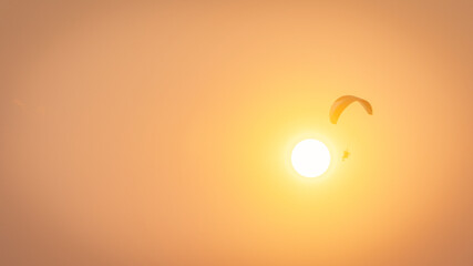 The silhouette of the pilot controlling a paramotor, flying over the orange sky at sunset