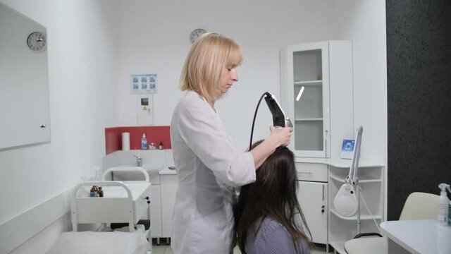 The trichologist performs an analysis of the hair on the patient's head in a cosmetology clinic.