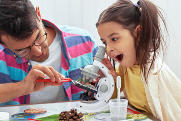 Amazed little girl looking trough the microscope dicovery nature with father at home. Dad and...