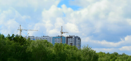 Construction of an apartment building. Green Forest. High-altitude cranes. Panel technology for building construction. Cumulus sky.