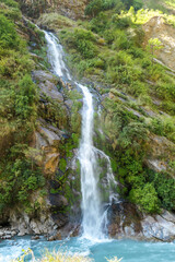 Obraz na płótnie Canvas A waterfall spotted in Tal, Annapurna Circuit Trek, Nepal. Few hundred meters of free fall, waterfall surrounded by tall mountains slopes, covered with green bushes and trees. Smooth capture