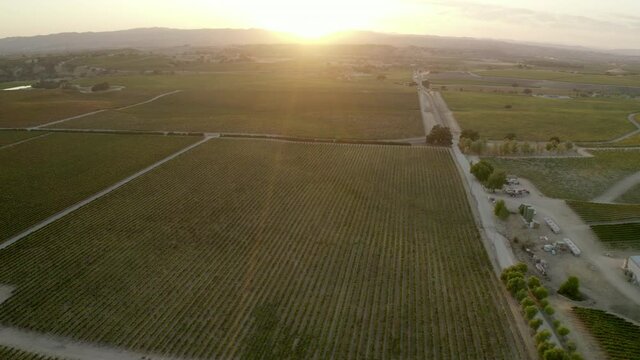 Aerial panning shot of agricultural field with structures and vehicles at sunset, drone flying over vineyard against sky - Paso Robles, California