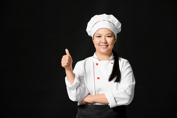 Beautiful Asian chef showing thumb-up gesture on dark background