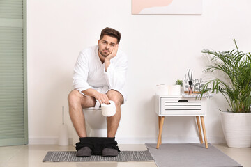 Young man sitting on toilet bowl in restroom