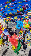 Naklejka premium A man standing between prayer flags at the top of Thorung La Pass, Annapurna Circuit Trek, Nepal. He is very happy. Colorful prayer flags attached to the stone wall, blown by the wind. Clear sky.
