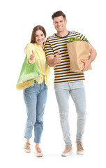Couple with food in bags showing thumb-up gesture on white background