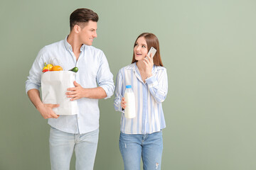 Couple with food in bag and mobile phone on color background