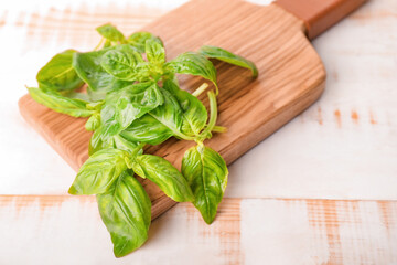 Cutting board and fresh green basil on wooden background