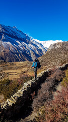 Naklejka premium Man standing at a stony wall while trekking Annapurna Circus, Himalayas, Nepal, with the view on Annapurna Chain. Dry and desolated landscape. High, snow capped mountain peaks. Happiness and adventure