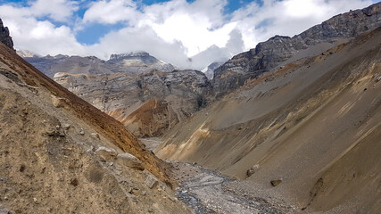 A small torrent flowing in Manang Valley, Annapurna Circus Trek, Himalayas, Nepal, with the view on Annapurna Chain. Dry and desolated landscape. High, snow capped mountain peaks.