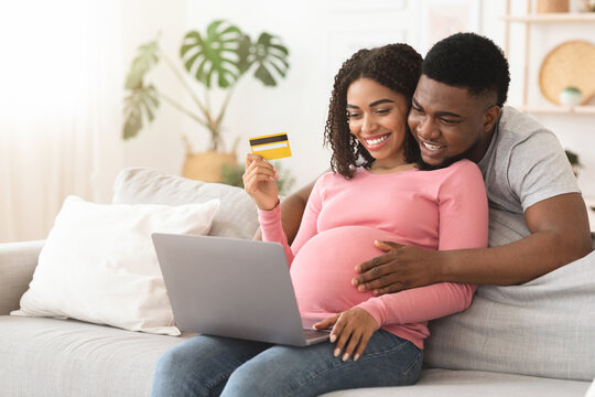 Happy expectant african american couple shopping online, using laptop