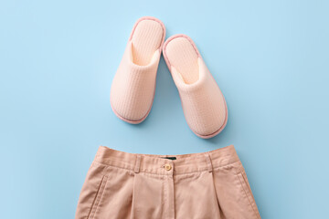 Pair of soft slippers and clothes on color background
