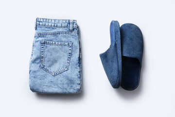 Pair of soft slippers and jeans on light background