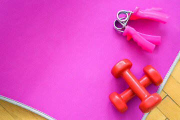 Top view of fitness equipment - pink mat for workout, two red dumbbells. Concept of training. Copy space.