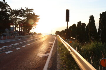 道路に朝日が昇り眩しい風景