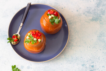 Traditional Spanish soup gazpacho with cucumber and tomato garnish. Summer homemade cold tomato cream soup in glass jars. Grey concrete background. Top view.