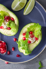 Avocado with pomegranate seeds, ricotta or cream cheese, lettuce leaves and mint on a blue ceramic plate. Healthy organic vegetarian diet food. Top view. Close up.