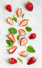 Flat lay composition with whole and sliced strawberries and mint leaves on a light grey stone background. Summer background composition. Top view.