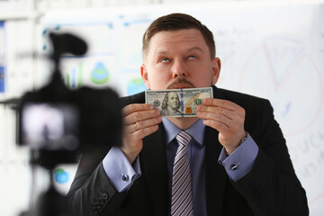 Male in suit and tie dollar banknote making promo videoblog or photo concept in office camcorder to...