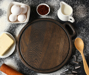 eggs, cocoa, milk, flour, butter and cooking supplies around the wooden cutting board. baking preparation