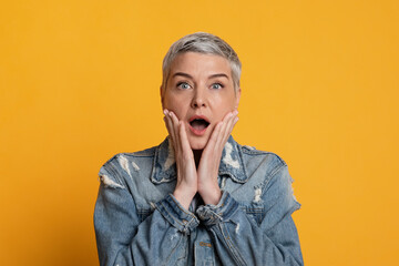 Unbelievable Offer. Shocked middle aged woman touching face in amazement, yellow background