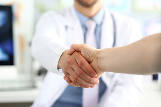 Focus on male shaking hands. Physician wearing white uniform and stethoscope. Men demonstrating welcome and friendly gesture. Medical treatment and health care concept. Blurred background