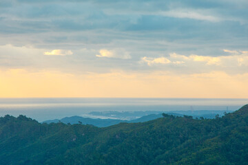 The view from the top of the hill from afar shows the sunrise of the sea and land where the rain clouds are clearing.