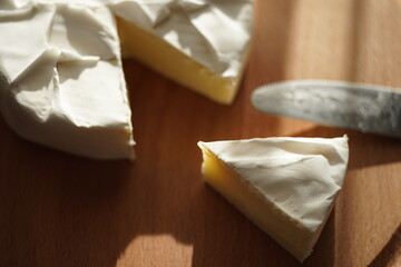 Camembert cheese slice and whole with knife end on a wooden board