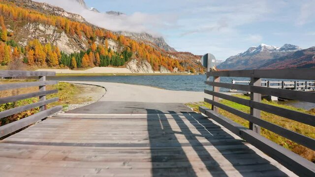 4k drone forward video (Ultra High Definition). Wooden bridge in the park on the shore of Sils Lake (Silsersee). Colorful morning view of Swiss Alps, Maloja Region, Upper Engadine, Switzerpand, Europe
