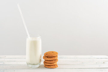 milk in a glass goblet with a straw on a white background. stack of oatmeal cookies