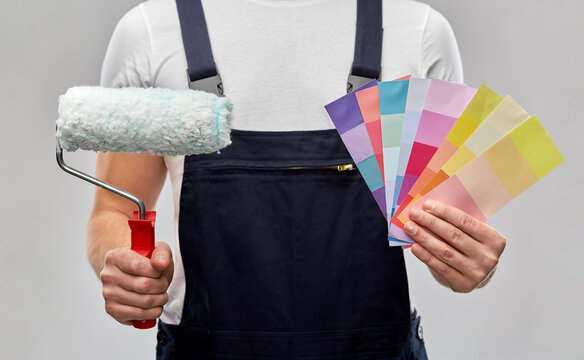 repair, construction and building - close up of painter or builder with paint roller and color charts over grey background