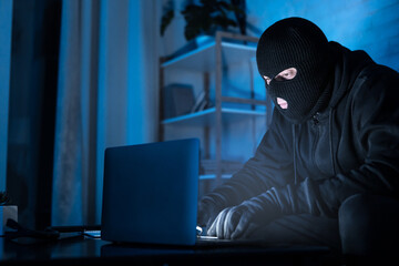 Masked hacker downloading private information using pc