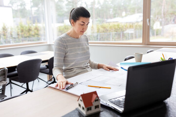 remote job, business and people concept - young female architect with blueprint of house project and laptop computer working at home office