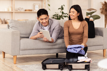 Asian Couple Using Tablet Packing For Vacation Sitting At Home
