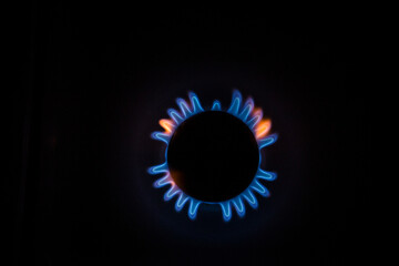 isolated close up shot of a blue and orange circular fire with small flames on the perimeter coming from a kitchen gas stove and forming a silhouette of an angel or a turtle on a black background