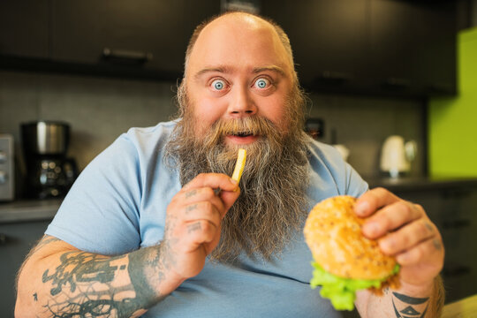 Close up of enthusiastic blue-eyed man with burger and french fries