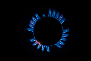 isolated close up shot of a blue and orange circular fire with small flames on the perimeter coming from a kitchen gas stove and forming a silhouette of an angel or a turtle on a black background